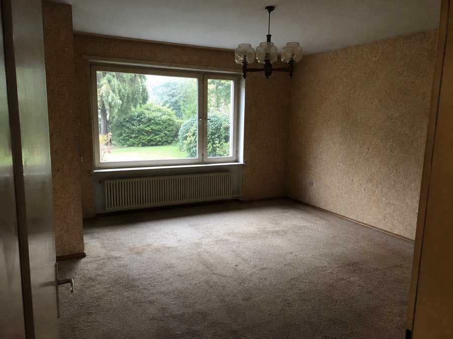 Leerer Wohnraum mit Teppichboden und großem Fenster zum Garten